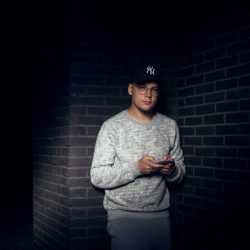 Spotlice CEO Jacob Michalak stands holding a phone before a brick wall,.